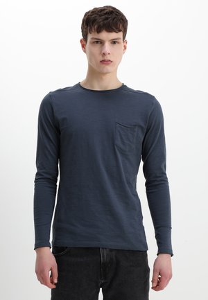Chemise à manches longues navy avec col rond, dotée d'une poche avant et d'un tissu doux et léger. La coupe est décontractée, associée à un jean foncé.