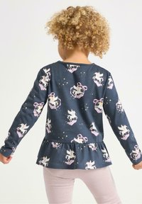 Tummansininen pitkähihainen paita peplum-tyylillä, jossa on yksisarviskuvio ja hopeisia tähtiä. Pehmeää puuvillamateriaalia ja pyöreä pääntie.