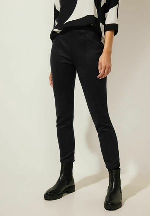 Pantalons noirs slim en tissu doux et extensible. Présentent une texture lisse et une taille sans fermetures visibles. Associés à des bottines noires.