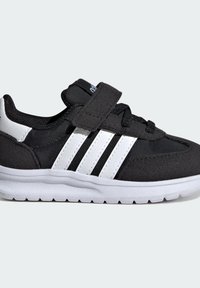 Černá sportovní bota s suchým zipem, bílými pruhy a bílou gumovou podešví. Kombinace textilních a syntetických materiálů.
