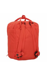 Zaino in tessuto rosso con spallacci regolabili, manico superiore, tasca frontale e dettagli in metallo nero. Design di forma quadrata.