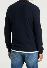 Pull en maille côtelée bleu marine à manches longues, avec un col rond et un ourlet droit, porté sur un jean en denim bleu clair.