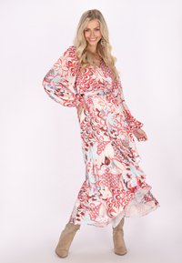 Rochie lungă și vaporoasă, cu un model floral în nuanțe de roz, roșu și albastru deschis. Are mâneci largi, decolteu în formă de V și tiv ondulat. Asortată cu cizme neutre.