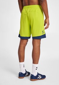 Klart limegröna träningsshorts med en marinblå fåll, elastisk midja och Hummel-logotyp på sidan, med en slät textur.