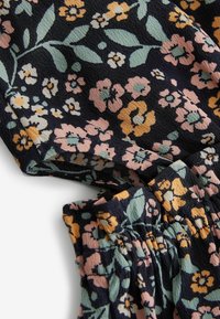 Kwiatowy materiał z różowymi, żółtymi i zielonymi kwiatami na granatowym tle. Teksturowana powierzchnia z marszczonymi detalami wzdłuż krawędzi.