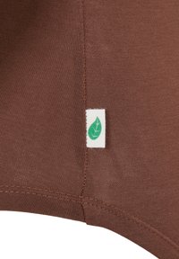 Smeđi materijal s glatkom, teksturiranom završnom obradom. Ima bijelu etiketu s logotipom zelenog lista pričvršćenom na bočnu šav.