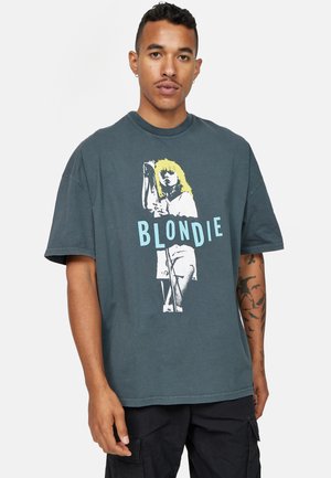 Šedé oversized tričko vyrobené z bavlny; obsahuje retro grafický potisk postavy s blond vlasy a modrý nápis "BLONDIE".