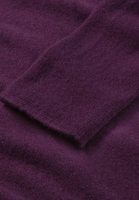 Lila gestrickter Stoff, der eine weiche Textur mit einem gerippten Bündchen zeigt, ausgestattet mit einem glatten, leicht flauschigen Finish und einer einheitlichen Farbe throughout.