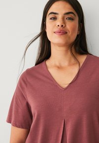 Bordeaux V-hals t-shirt met korte mouwen, met een centrale plooi detail en een gladde, lichtgewicht textuur. Eenvoudig ontwerp zonder patronen.