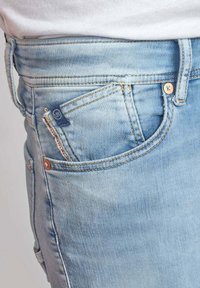 Jeans de mezclilla azul claro con una cintura de altura media, que cuentan con bolsillos frontales, costuras en contraste y una pequeña etiqueta de marca en el bolsillo para monedas.