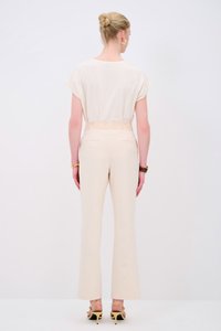 Beige, luchtige top met korte mouwen en crèmekleurige, hooggetailleerde broek. Opvallende, gestructureerde tailleband en gele, hoge hakken zijn zichtbaar.