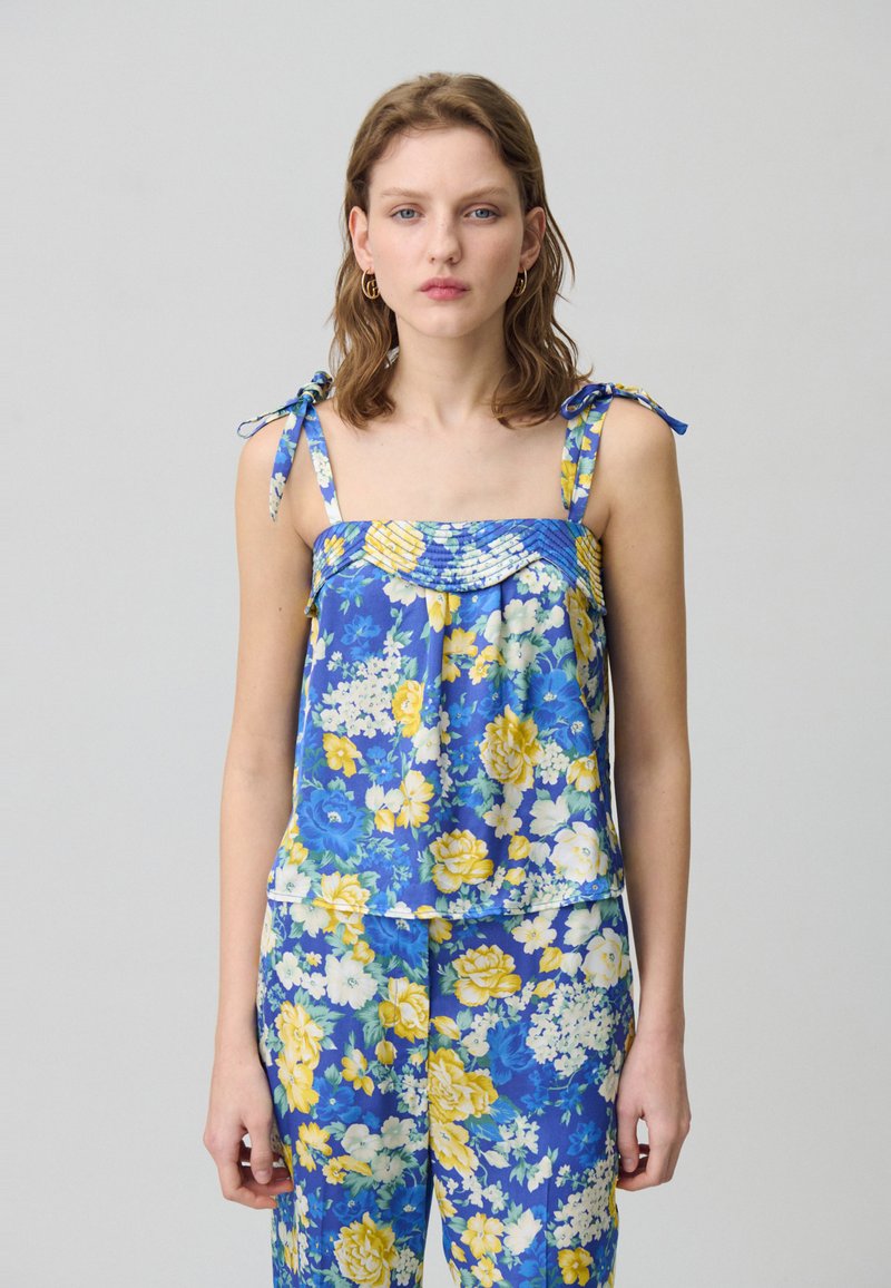 Completo floreale a due pezzi con sfondo blu e fiori gialli e bianchi. La parte superiore ha spalline sottili e un colletto arricciato.