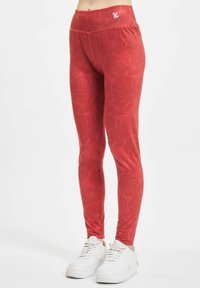 Leggings rossi con un motivo floreale testurizzato, vita alta e dettaglio del logo; abbinati a sneaker bianche con lacci.