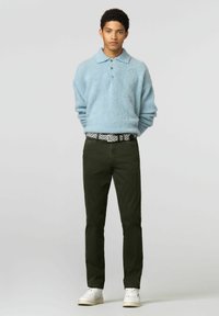 Lichtblauw, pluizig shirt met een kraag en drie knopen, gecombineerd met donkergroene broek en een riem met patroon, afgewerkt met witte sneakers.