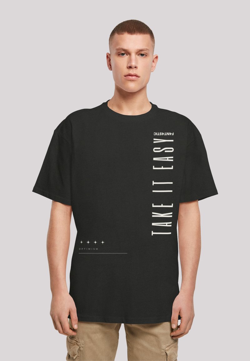 Black cotton t-shirt with oversized fit. Front features vertical white text "TAKE IT EASY" and graphic accents. Short sleeves, round neckline.