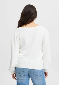 Weißer Pullover mit Rundhalsausschnitt, gerippten Bündchen und glatter Textur. Kombiniert mit hellblauen Jeans in lässiger Passform.