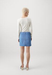 Svetlo siva majica dugih rukavov v kombinaciji z modrim denim krilom. Krilo ima ravno krojenje in zvit rob, nosi pa se s bež čevlji na blok peto.