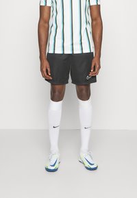 Zwarte Nike shorts, wit gestreept shirt met blauwe en zwarte accenten, witte sokken en multikleurige Nike voetbalschoenen.