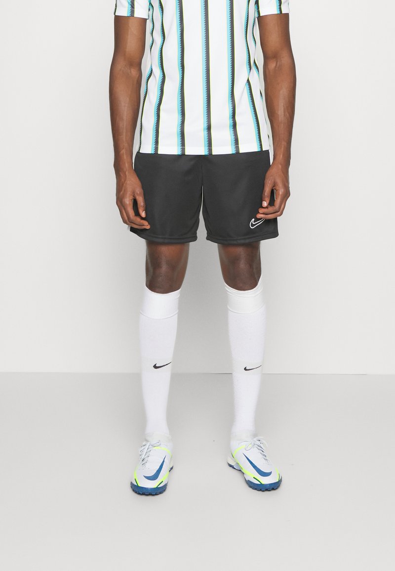 Zwarte Nike shorts, wit gestreept shirt met blauwe en zwarte accenten, witte sokken en multikleurige Nike voetbalschoenen.
