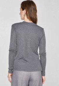 Grau langärmliges Shirt aus weichem Stoff, mit rundem Halsausschnitt und körpernahen Ärmeln, getragen mit hellen Hosen.