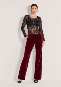 Zwarte kant lange mouw bodysuit, gelaagd over een zwarte bh, gecombineerd met hoogophaal burgundy fluwelen wijde broek. Zwarte open teen hakken.