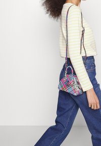 Karierte Handtasche in leuchtenden Pink-, Blau- und Gelbtönen, mit dreieckiger Form, zwei kurzen Griffen und einem abnehmbaren Schultergurt.