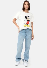 Hvid kortærmet t-shirt med et stort trykt grafisk motiv af Mickey Mouse, parret med lyseblå jeans og hvide sneakers.