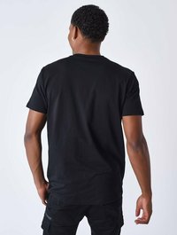 Camiseta negra de cuello redondo hecha de algodón, con mangas cortas. Costuras visibles y corte recto en el dobladillo.