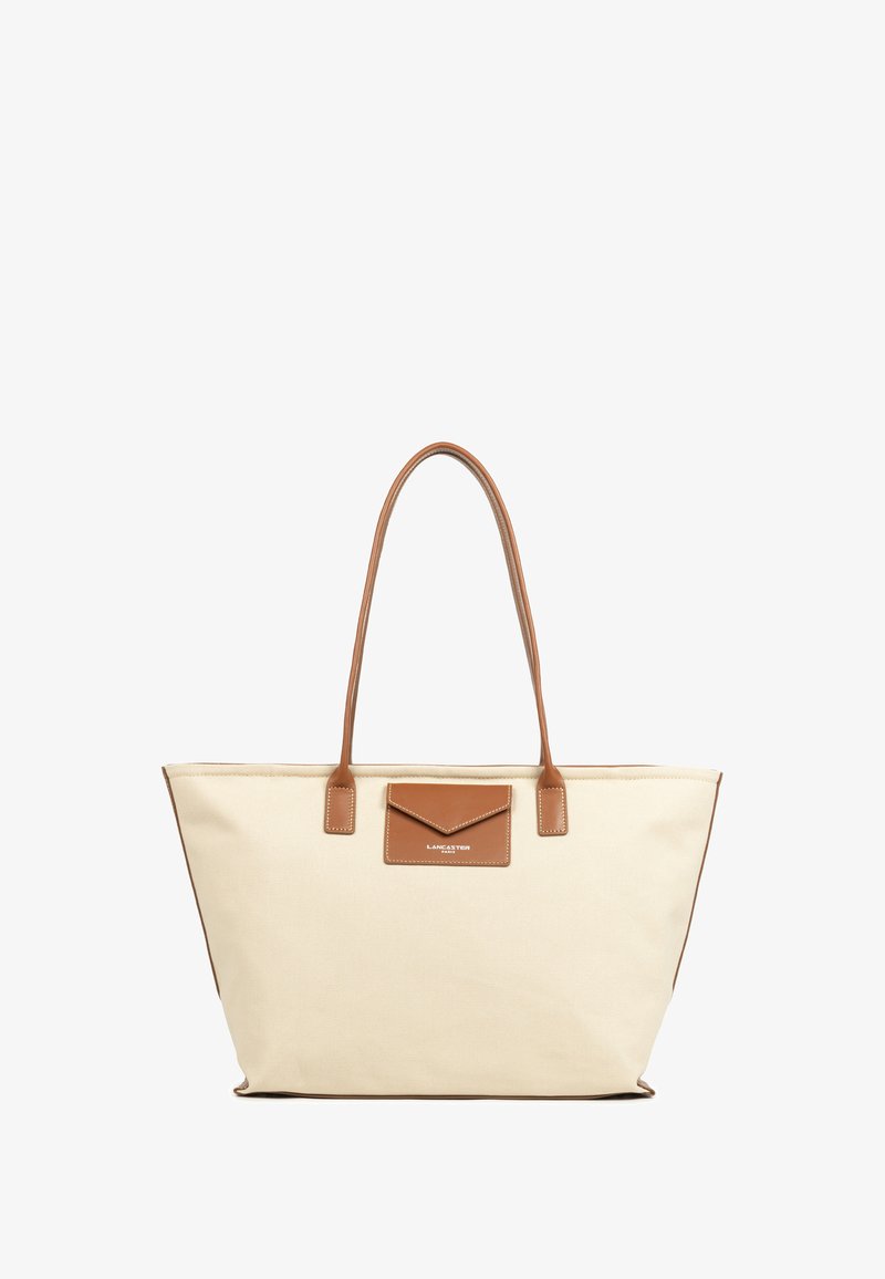 Canvas draagtas in off-white met bruine leren accenten. Voorzien van twee lange handvatten en een voorvak. Gestikte details langs de randen.