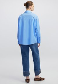 Lichtblauwe oversized shirt met een puntige kraag, lange mouwen en knoopmanchetten, gecombineerd met opgerolde denim jeans en schoenen met luipaardprint.