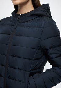 Μπλε ναυτικό μπουφάν puffer με εφαρμοστή σχεδίαση, οριζόντια ραφή, κουκούλα και μπροστινό φερμουάρ. Λείο και λαμπερό υλικό.