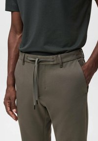 Gray-green pants with a subtle texture, featuring a drawstring waist and side pockets, paired with a dark t-shirt.