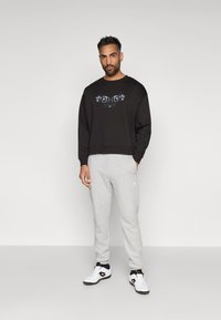 Sweatshirt preto curto com design gráfico, combinado com calças de moletão cinza claro e sapatos atléticos brancos. Corte simples e relaxado.