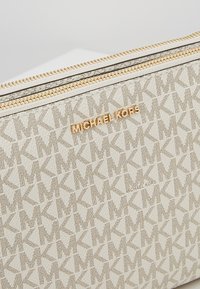 Michael Kors patroonetui in beige, met een logo-design, gouden rits en een gestructureerd oppervlak. Voorzien van geperst merkdetail.