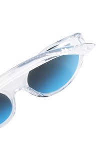 Las gafas de sol claras y de gran tamaño presentan lentes de degradado azul oscuro, una forma angular de ojo de gato y montura transparente de textura suave con acentos decorativos.