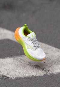 Chaussure de course avec une tige en mesh blanc, des accents vert lime et un talon orange. Comprend un col rembourré et une semelle extérieure texturée pour une meilleure adhérence.