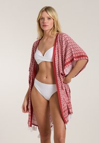 Sarkans raksts kimono ar brīvu piegriezumu, ar frizūru akcentiem. Valkāts virs baltas bikinī augšdaļas un ribota bikinī apakšdaļas.