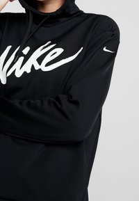 Felpa nera con cappuccio realizzata in tessuto morbido, presenta un grande logo bianco "Nike" e uno swoosh Nike bianco sulla manica. Include un cappuccio regolabile con cordino.