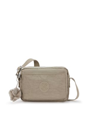 Beige crossbody taske med tekstureret stof, lynlås og en frontlomme. Har en rund logo og en pelsagtig nøglering.