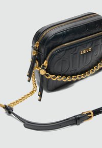 Czarna skórzana torba crossbody z dwoma zamykanymi na zamek komorami, złotym detalem w postaci łańcuszka oraz wytłoczonym logo. Regulowany pasek i gładka tekstura.