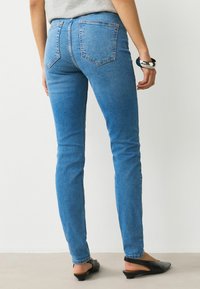 Modré džíny slim fit z denimu, s vysokým pasem, dvěma zadními kapsami a čistým provedením. Kombinovány s černými botami na patu.