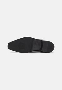 Black dress shoe sole featuring a smooth rubber texture, a pointed toe, and embossed logo detail. Medium width with a flat design.