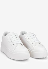 Sneakers bianchi in pelle con lacci piatti, suole a zeppa, punta tonda e dettagli di cucitura sottili. Texture liscia e design minimalista.