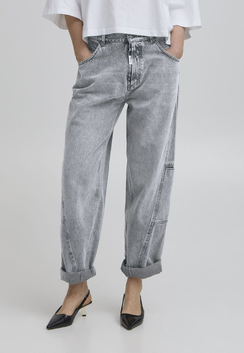 Gray denim jeans with a relaxed fit, featuring side pockets and cuffed hems, paired with black pointed-toe heels.