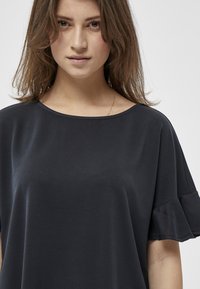 Zwart top met een wijde halslijn en gerimpelde korte mouwen. Gemaakt van gladde stof; minimalistisch ontwerp zonder zichtbare patronen of accenten.