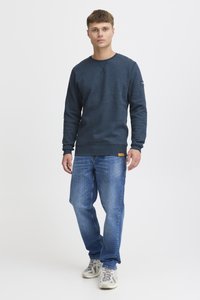 Sudadera azul marino de manga larga y cuello redondo, combinada con jeans de pierna recta azul claro y zapatillas beige con acentos grises.