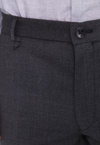 Pantaloni in misto lana grigi con una texture liscia, dotati di chiusura con bottone e design frontale piatto. Il tessuto presenta un delicato motivo intrecciato.