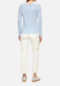 Un haut bleu clair à manches longues associé à un jean crème. Le haut a une encolure ronde et une texture lisse ; le jean présente un ourlet brut. Les baskets ont un accent gris.
