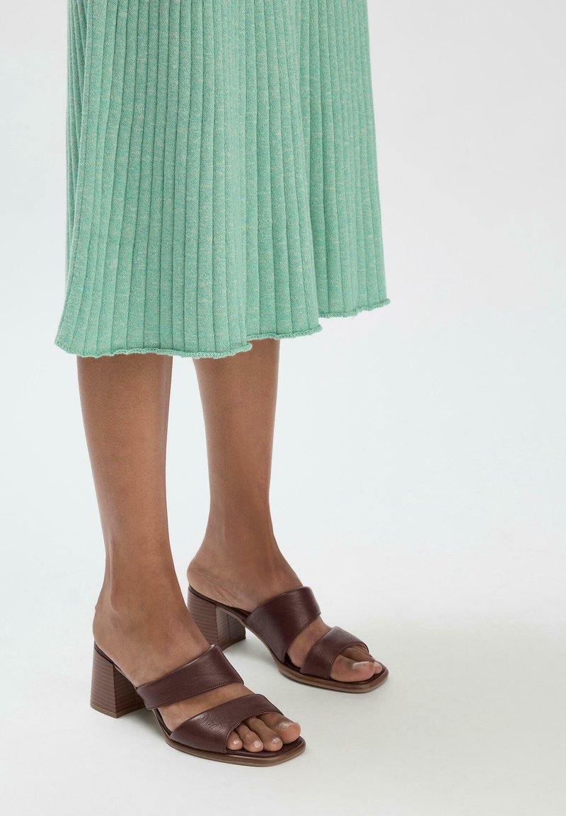 Bruine leren sandalen met blokhak en twee brede banden, gecombineerd met een geribbelde mintgroene jurk. Gladde textuur en open teenontwerp.