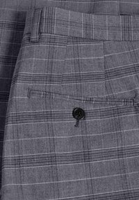 Pantalones de cuadros grises con frente plano, tela texturizada y un cierre de botón negro en un bolsillo trasero. Rayas horizontales y verticales visibles.